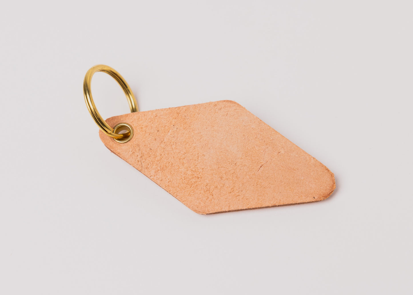 Backside of Besco leather motel keychain showing natural vegetable-tanned leather texture and brass key ring
