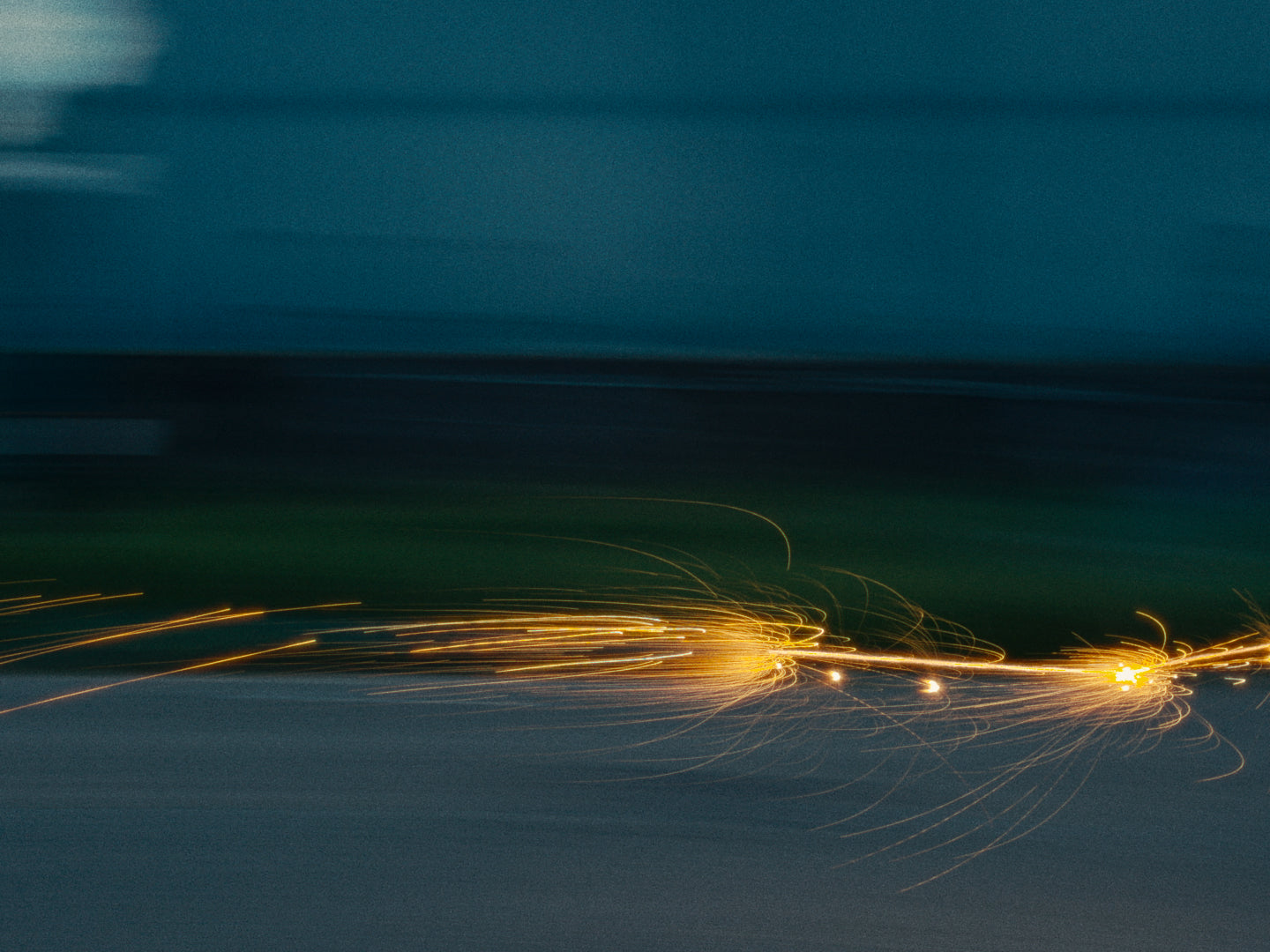 Long-exposure photo capturing golden fireworks streaking across a dark blue evening sky, creating flowing light trails.
