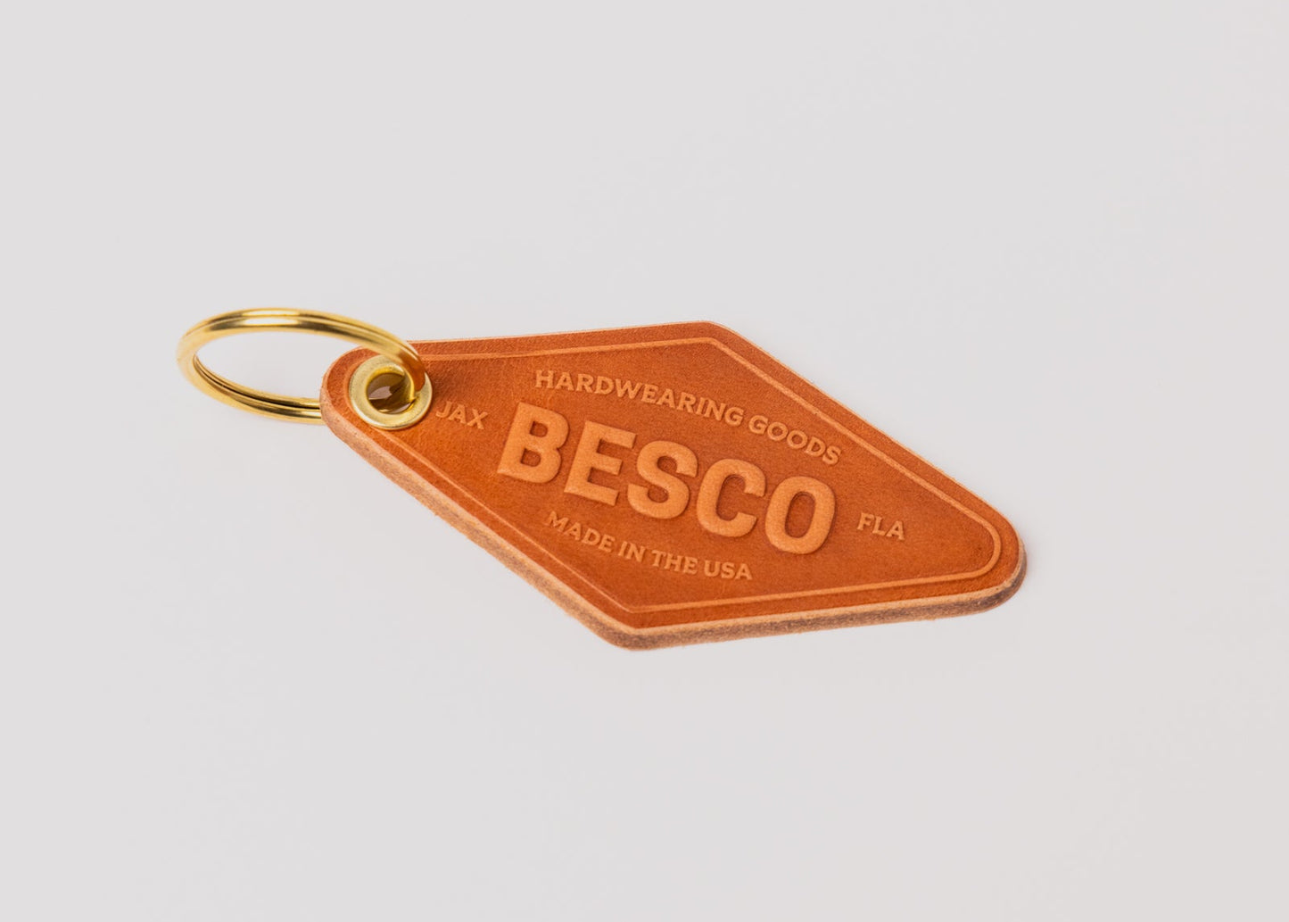 Besco leather motel keychain stamped 'Besco Hardwearing Goods Made in the USA JAX FLA' showing natural vegetable-tanned leather texture and brass key ring