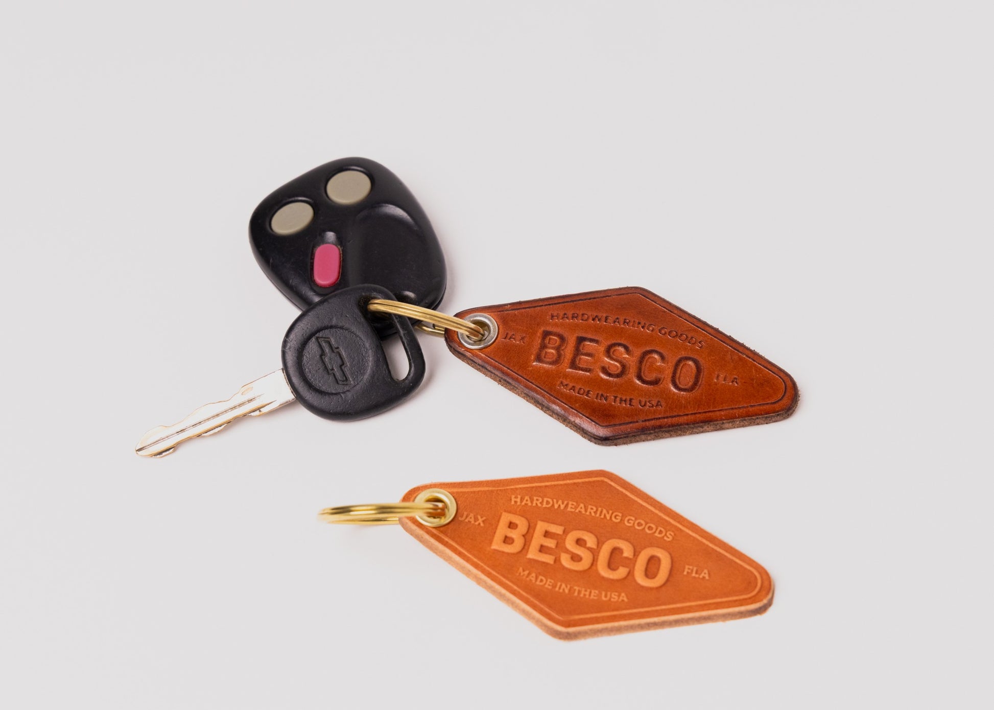 Two Besco leather motel keychains attached to car keys, showing new and aged versions side by side to highlight natural patina development of vegetable-tanned leather